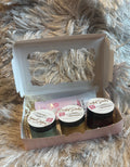 Three small jars in a cardboard box on a fluffy gray surface